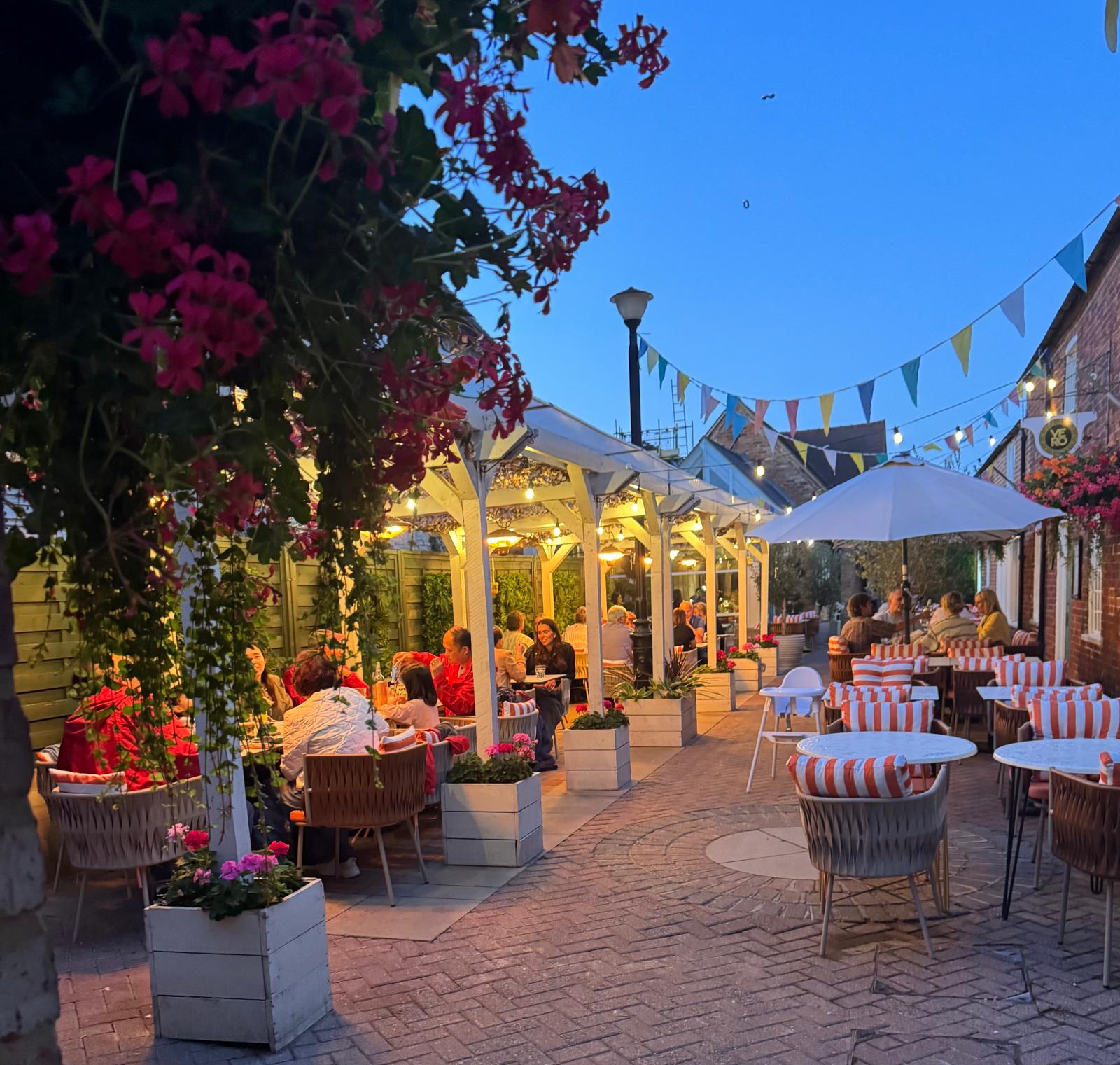 The Italiano Vero Terrazza courtyard at dusk with flowers, lights and outdoor tables